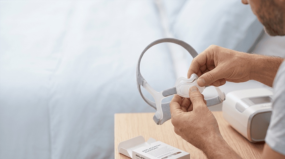 Person replacing nasal pillows on a CPAP mask beside a CPAP machine